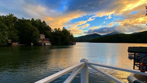 Vista sul lago da una barca con un molo, acqua calma e riva alberata.
