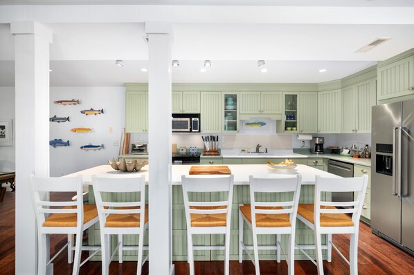 A modern kitchen with green cabinets, white countertops, and a central island with bar stools.