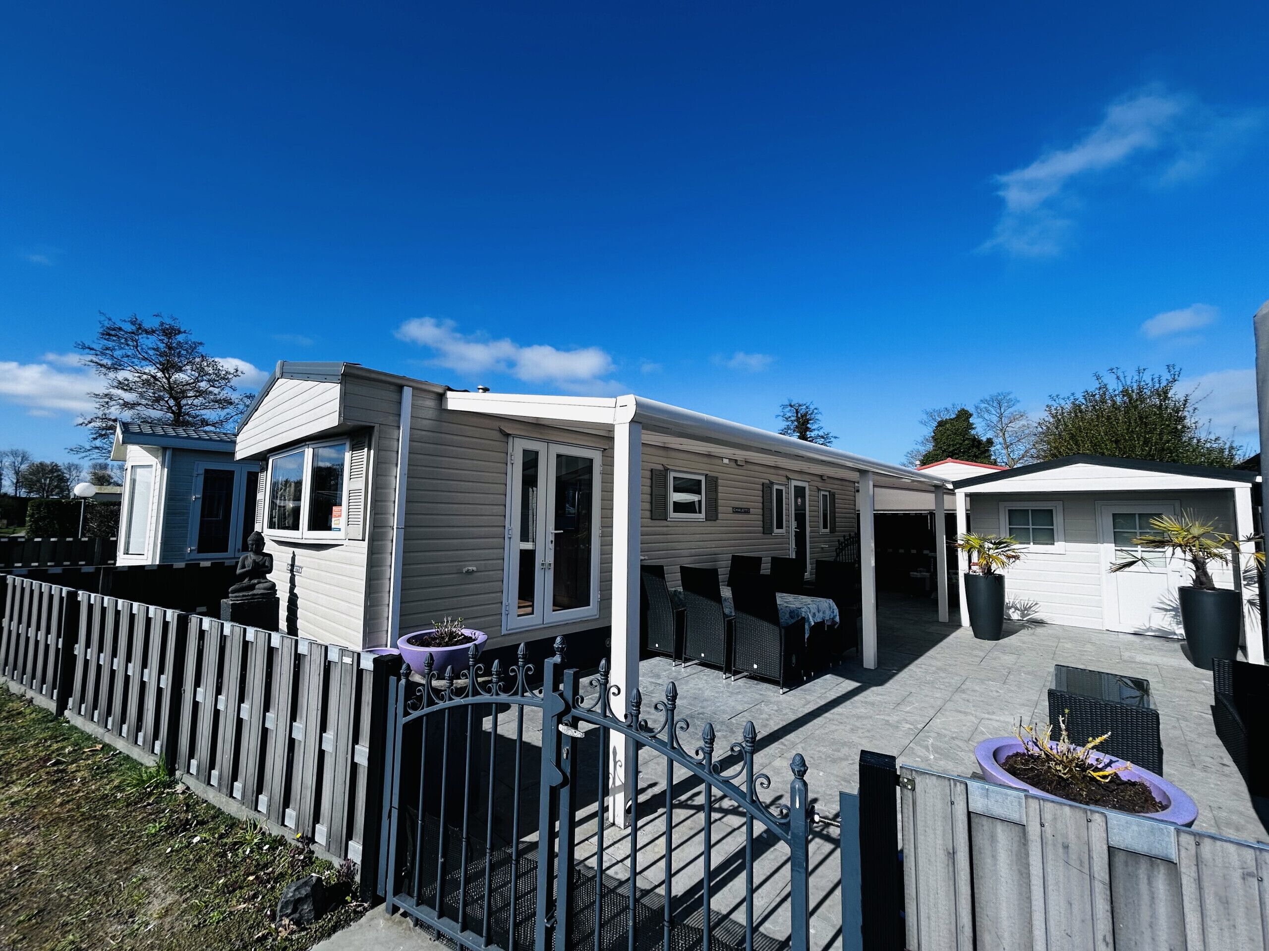 A mobile home with a patio area, a fenced yard, and a small garden.