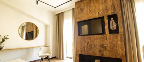 A modern bedroom with a large bed, a round mirror, a flat-screen TV, and a fireplace.
