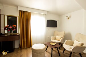 Una habitación de hotel moderna con suelo de madera, un escritorio con un florero, dos sillones, un pequeño reposapiés y un televisor de pantalla plana montado en la pared.