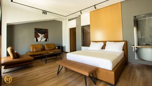 Et moderne hotelværelse med en stor seng, en sofa, en bænk og et badeværelse med badekar.