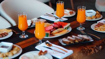 Mesa de café da manhã com diversos pratos, incluindo torradas, frutas e ovos, juntamente com copos de suco de laranja.