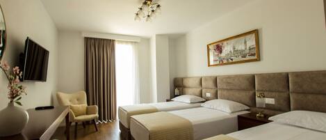 Habitación de hotel con dos camas, una silla, un escritorio con un florero, un cuadro en la pared y un televisor.