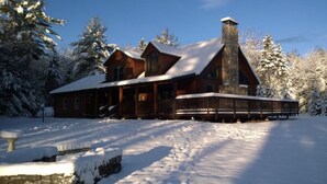 Een vakantiehuis van hout met een stenen schoorsteen, omgeven door met sneeuw bedekte bomen.