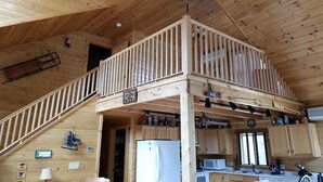 Een houten chalet met een slaapkamer op een entresol, een keuken met houten kasten, en een trap naar de entresol.