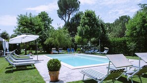 Ein Poolbereich mit Liegestühlen und Sonnenschirmen, umgeben von Bäumen.