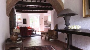 Ein gemütliches Wohnzimmer mit einem rustikalen Backsteinbogen, einem gemusterten Teppich und einem Tisch mit Lampe und Blumen.