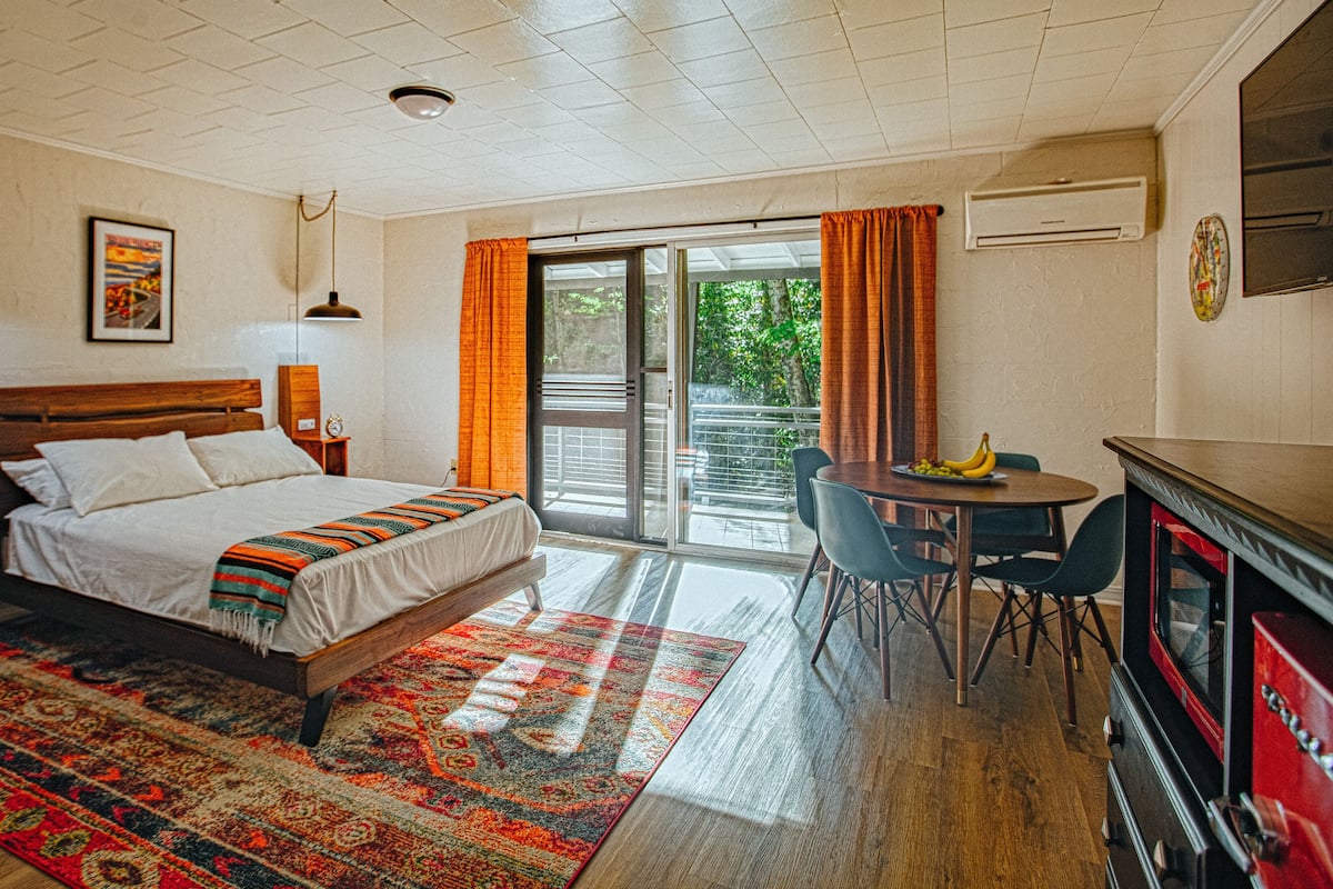 Ein Schlafzimmer mit einem Bett, einem Schreibtisch, Stühlen, einem roten Schrank und Blick ins Freie.