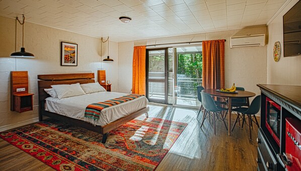 A bedroom with a bed, a desk, chairs, a red cabinet, and a view of the outdoors.