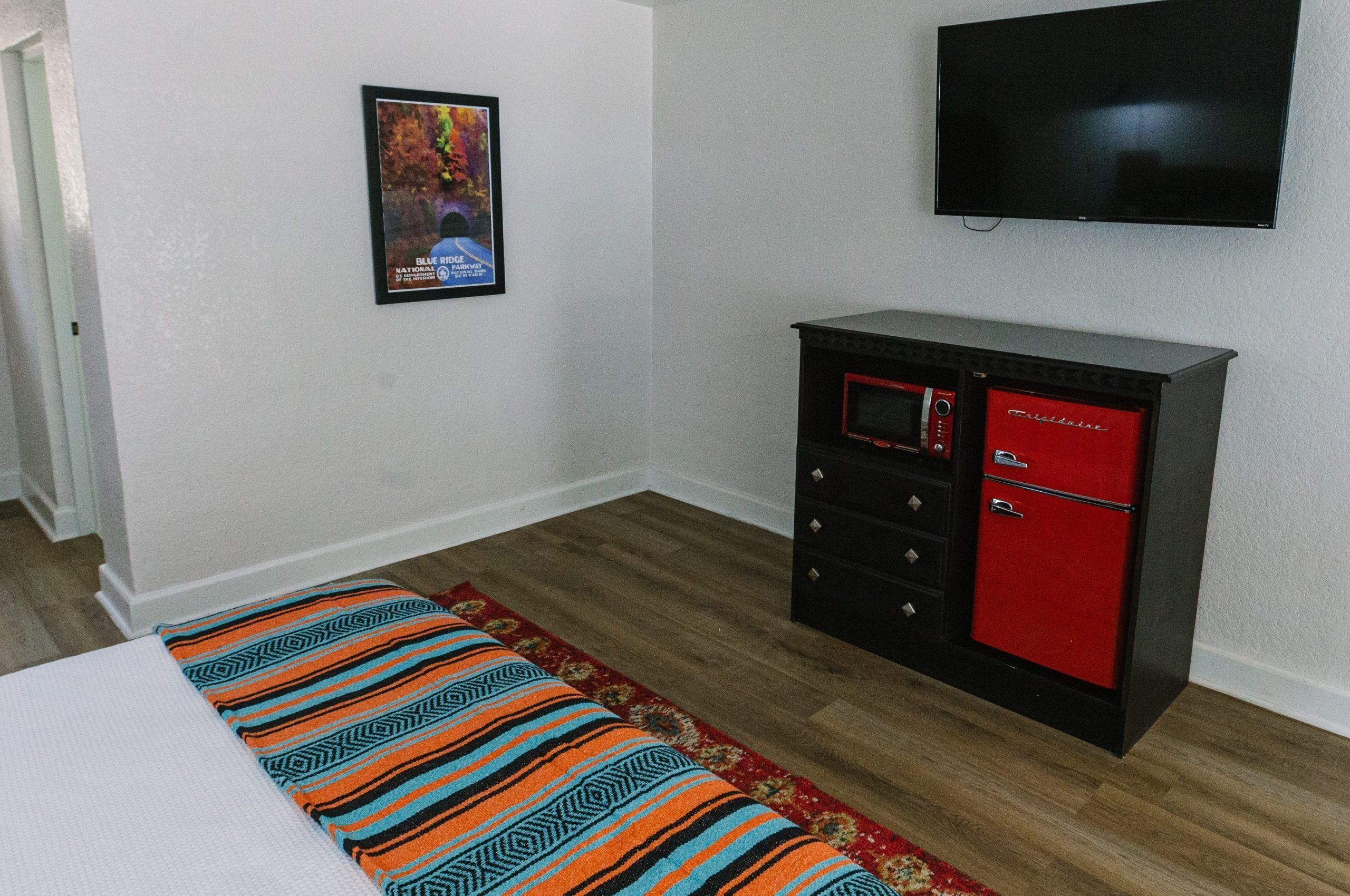 A room with a bed, a TV mounted on the wall, a red and black cabinet, and a poster on the wall.