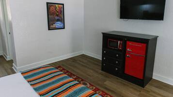 A room with a bed, a TV mounted on the wall, a red and black cabinet, and a poster on the wall.
