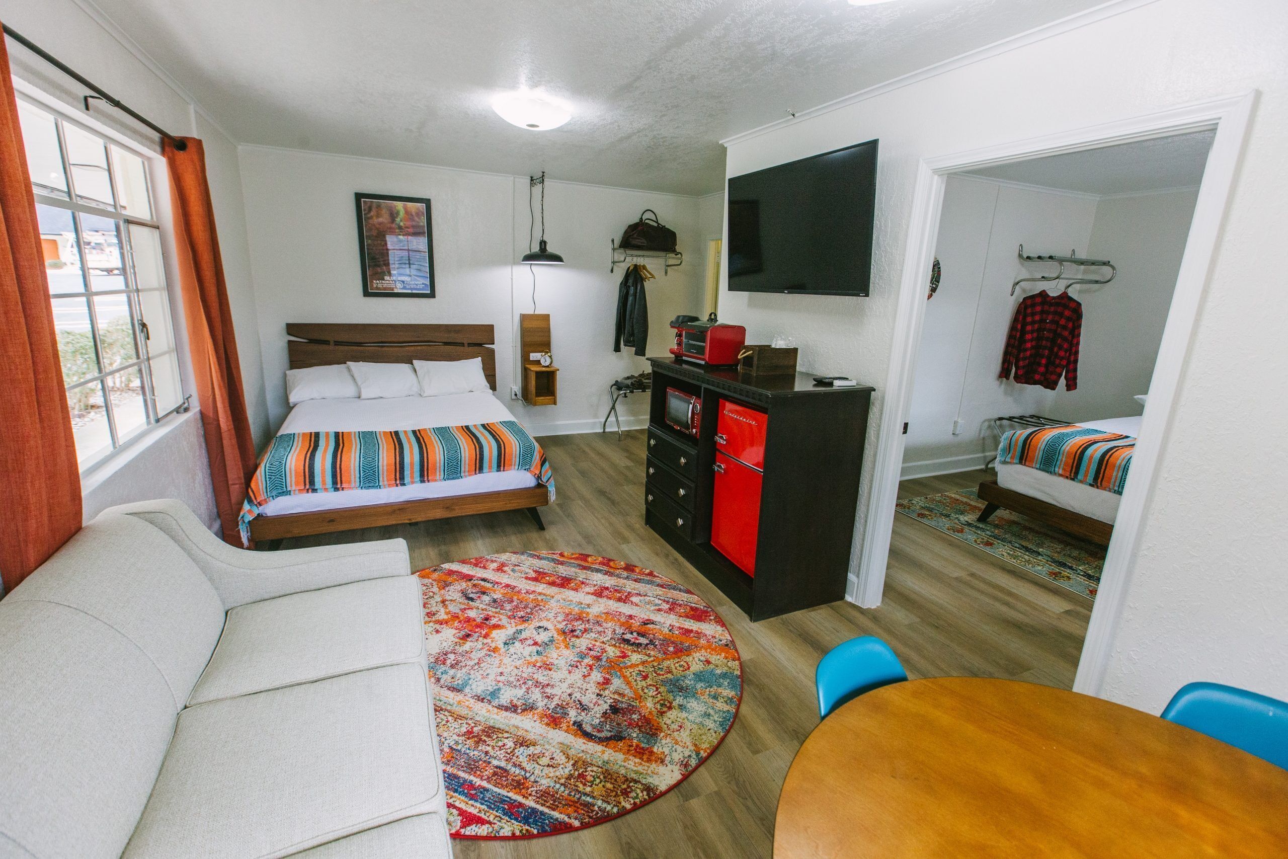 A compact hotel room with a bed, a sofa, a dining table, and a TV.