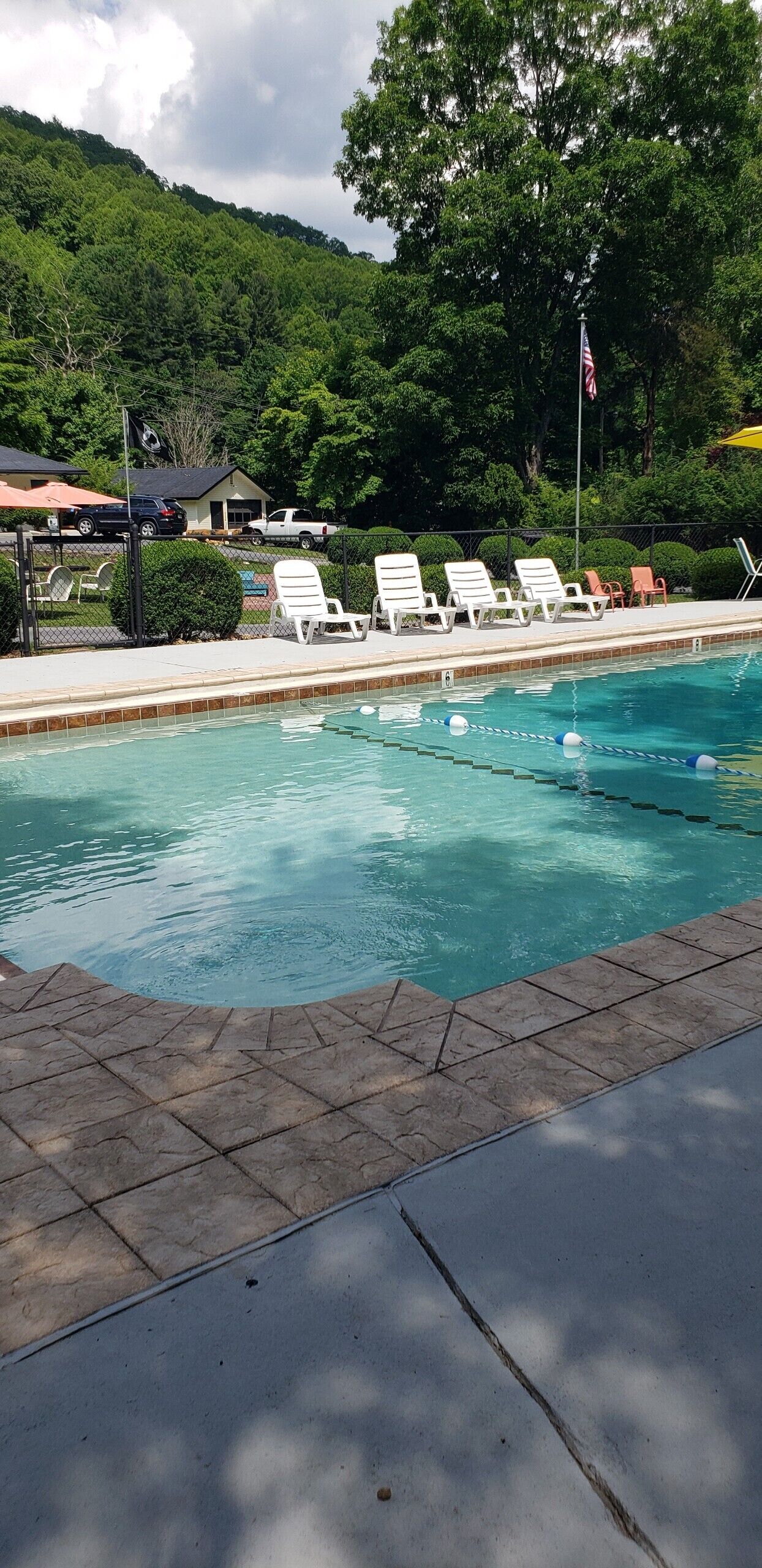 A swimming pool with lounge chairs, a flag, and a view of a green hill.