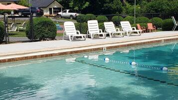 A swimming pool with lounge chairs, a flag, and a view of a green hill.