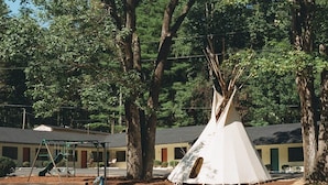 A teepee in a park with a playground and a building in the background. - Route 19 Inn (Maggie Valley)