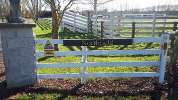 A white metal gate with a sign that reads "Northfield" and a warning sign about surveillance camera operation.
