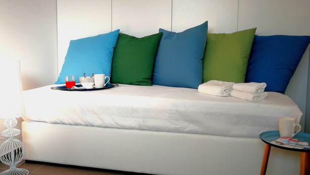 A neatly made bed with a white mattress, blue and green pillows, and a tray with a cup and a glass. - Villa Arillà: pool, padel, sea and relaxation (Marina di Ragusa)