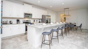 A modern kitchen with white cabinetry, stainless steel appliances, and a central island with bar stools. - 8905 New Luxury Solara Resort Private Pool (Kissimmee)