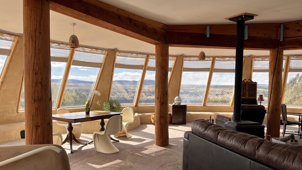 Une pièce aux hauts plafonds, dotée de grandes fenêtres, d’un sol en pierre, d’une table en bois avec des chaises, d’un canapé et d’une cheminée.