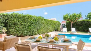 Un espace repas avec vue sur la piscine, du mobilier d’extérieur et une haie soigneusement taillée.