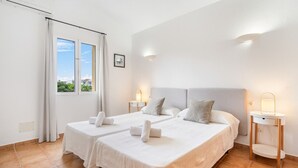 Une chambre d’hôtel avec deux lits, une grande fenêtre avec des rideaux, une table de chevet avec une lampe et un luminaire fixé au mur.