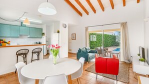 Une cuisine moderne aux armoires de couleur turquoise, un coin repas avec des chaises blanches et un salon avec un canapé rouge et un divan vert.