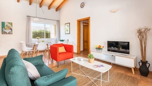 Una sala moderna con un sofá verde, un sillón rojo, una mesa de centro blanca, un televisor y un comedor con una mesa y sillas.