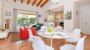 Un comedor amplio con una mesa redonda dispuesta para cuatro personas, sillas blancas y un sofá rojo al fondo.