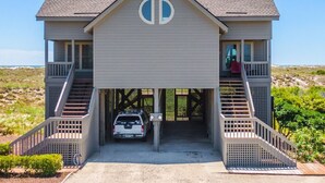 A two-story house with a garage entrance, a car parked inside, and a view of the beach. - Slow Motion | Community Beach Access + Pool! (Topsail Beach)
