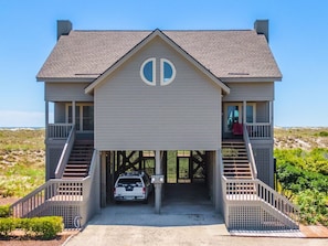 A two-story house with a garage entrance, a car parked inside, and a view of the beach. - Slow Motion | Community Beach Access + Pool! (Topsail Beach)