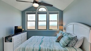 A bedroom with a bed, a dresser, a ceiling fan, and a window with a view of the beach. - Slow Motion | Community Beach Access + Pool! (Topsail Beach)