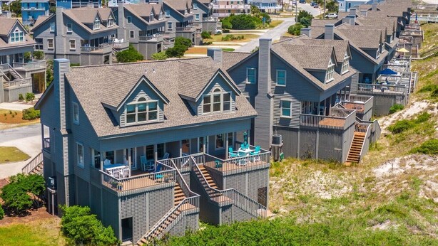A coastal residential area with houses featuring steep gabled roofs and a prominent staircase leading to a balcony. - Slow Motion | Community Beach Access + Pool! (Topsail Beach)