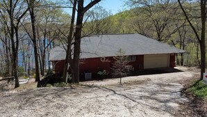 A single-story building with a red exterior and a grey roof, surrounded by trees and a gravel driveway. - Hog Heaven-Lower Level of Private Home- Lakefront (Garfield)