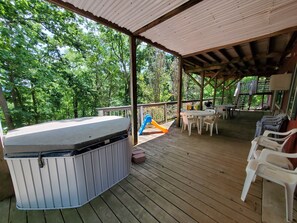 Une terrasse extérieure couverte, dotée d’un jacuzzi, de tables de pique-nique et de chaises, le tout entouré d’une végétation luxuriante.