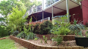 A two-story building with a balcony, surrounded by a variety of plants and a brick retaining wall. - Hog Heaven-Lower Level of Private Home- Lakefront (Garfield)