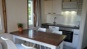 A compact kitchen with a wooden table, white chairs, a sink, a stove, and cabinets. - Beautiful vacation home in a quiet location (Mönchneversdorf)
