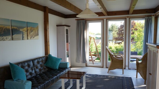 A room with a leather sofa, a table, wicker chairs, and a view of the outdoors through large windows. - Beautiful vacation home in a quiet location (Mönchneversdorf)