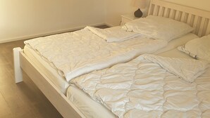 A neatly made bed with a white comforter and pillows, a bedside table with a lamp, and a painting on the wall. - Beautiful vacation home in a quiet location (Mönchneversdorf)