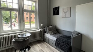Een moderne slaapkamer met een inbouwbed, een ronde tafel, een radiator en grote ramen met uitzicht op de straat.