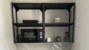 Een kleine keuken met een ingebouwde magnetron, een spoelbak en een koffiezetapparaat op het aanrecht.