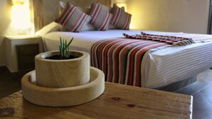 Un letto rifatto con lenzuola a righe, un comodino in legno con una pianta in vaso e una lampada da comodino.