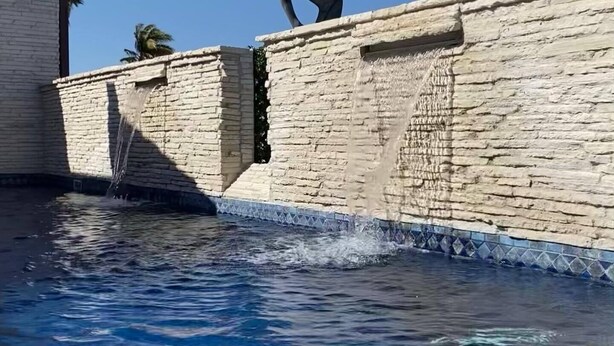 Una piscina con acqua cristallina, un muro di pietra e una scultura.