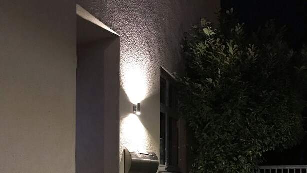 Entrada d'un edifici amb una caixa de correu il·luminada penjada a la paret, una escala de pedra i una barana metàl·lica.
