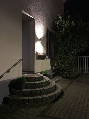 A building entrance with a lighted wall-mounted mailbox, a stone staircase, and a metal railing. - Small& fine with parking (Lüneburg)
