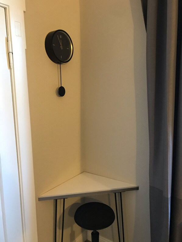 A corner room with a white wall, a black clock, and a small black table with a chair. - Small& fine with parking (Lüneburg)