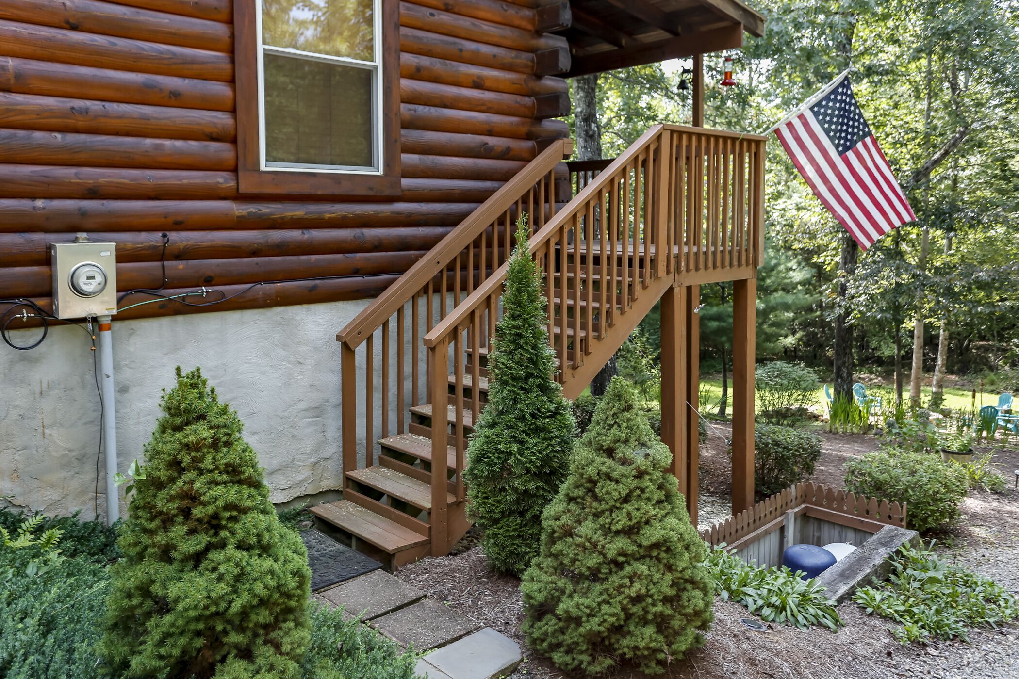 Een houten hutje met een houten trap naar een terras, omringd door groen en een Amerikaanse vlag.