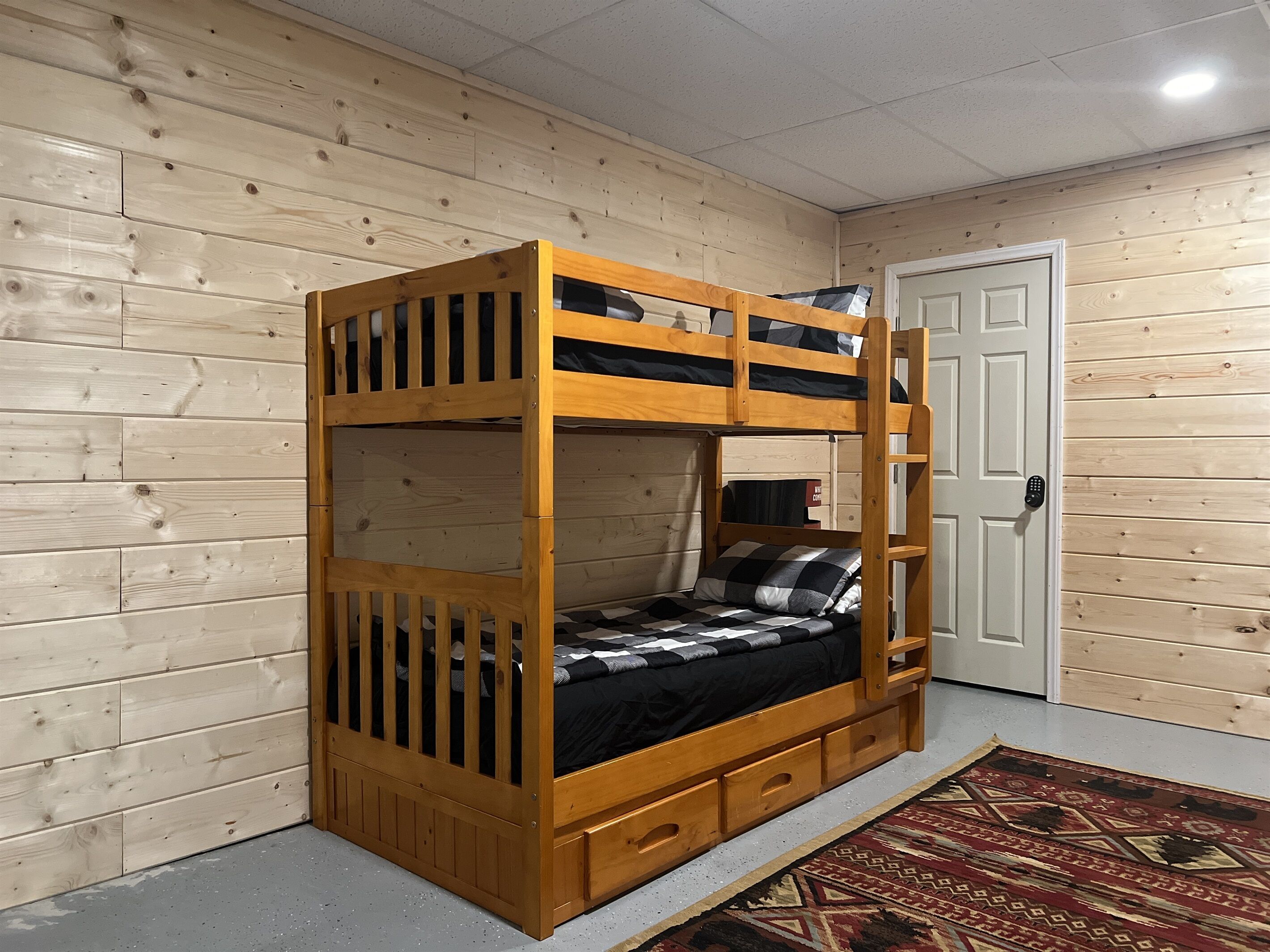 A bunk bed with a wooden frame and a lower bunk with a mattress and pillows. There is a door with a lock on the right side.