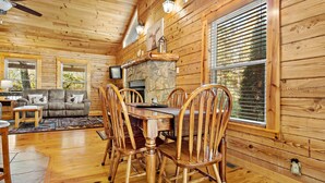 A wooden cabin interior with a dining table, chairs, a sofa, and a fireplace.