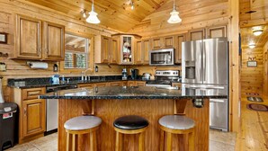 A kitchen with wooden cabinets, a stainless steel refrigerator, a microwave, and a large island with stools.